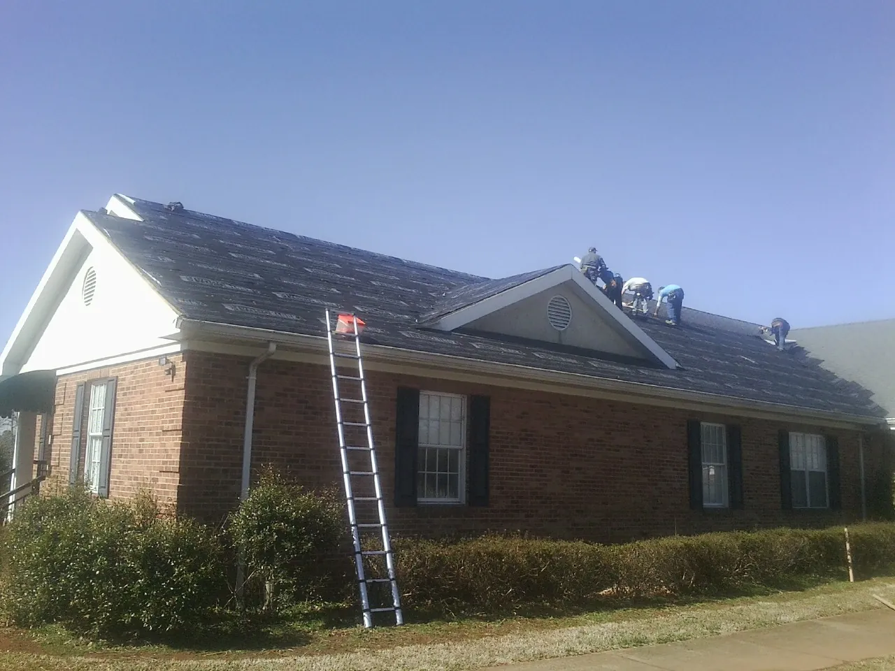 Crew tearing shingles off a brick ranch roof with a ladder set — Metal Roof Repair work by our crew in Pacolet