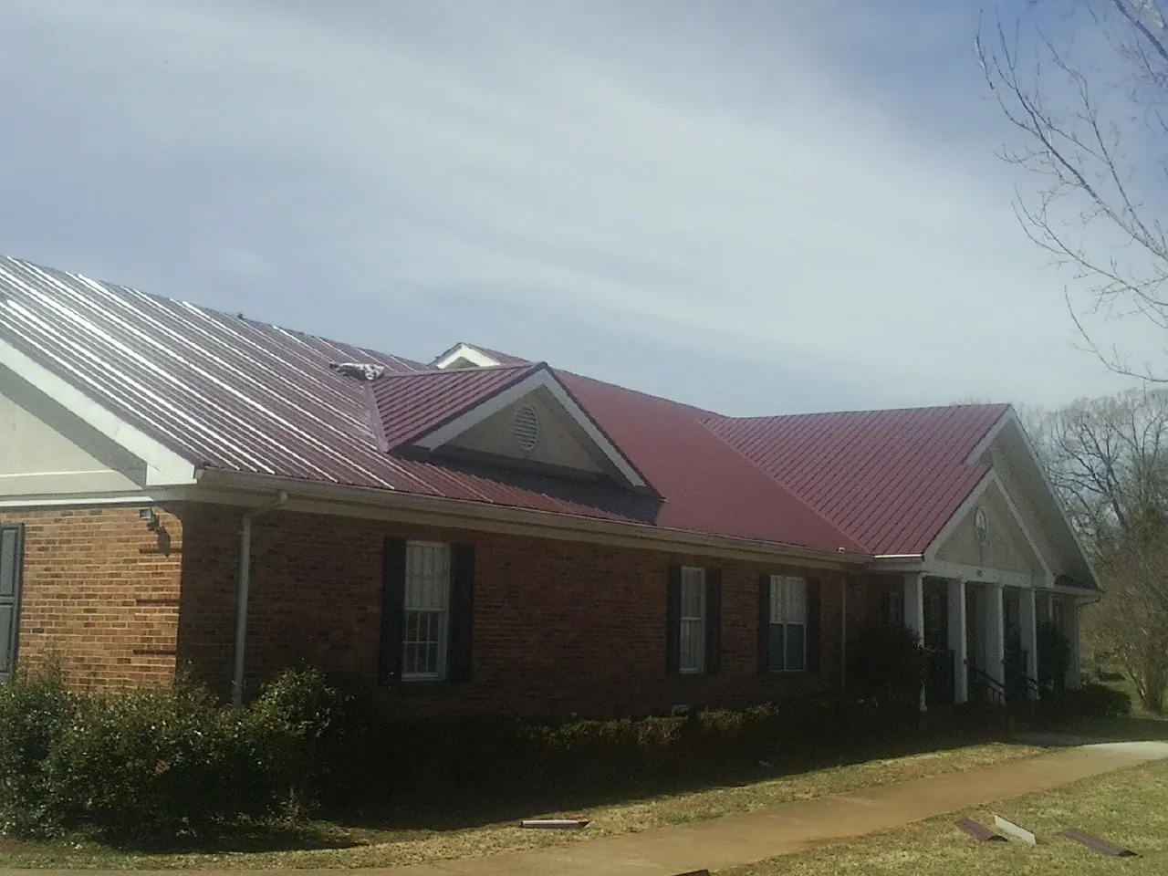 Red metal roof with gabled entries on a long brick building, from a Hail Damage Roof Repair job in Pacolet