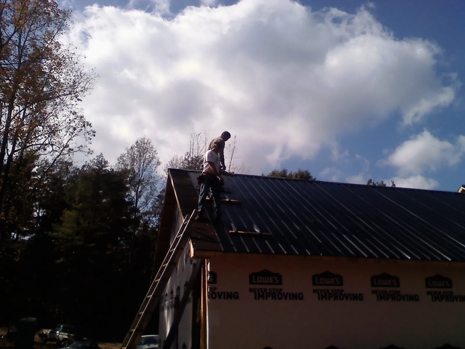 Roofer fastening dark metal panels high against a cloudy sky, from a Roof Inspection job in Pacolet