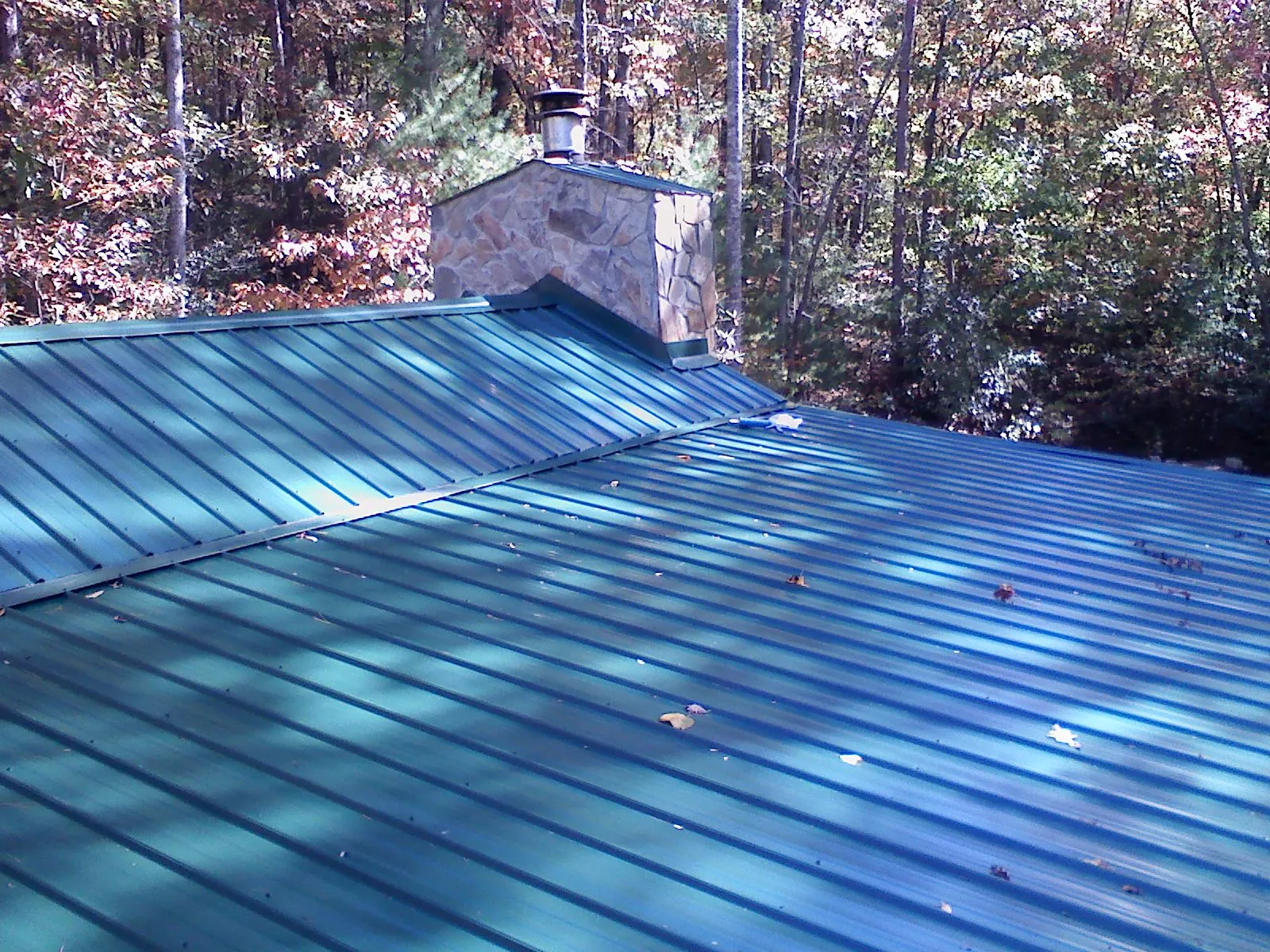 New green metal roof and stone chimney surrounded by autumn woods in Pacolet