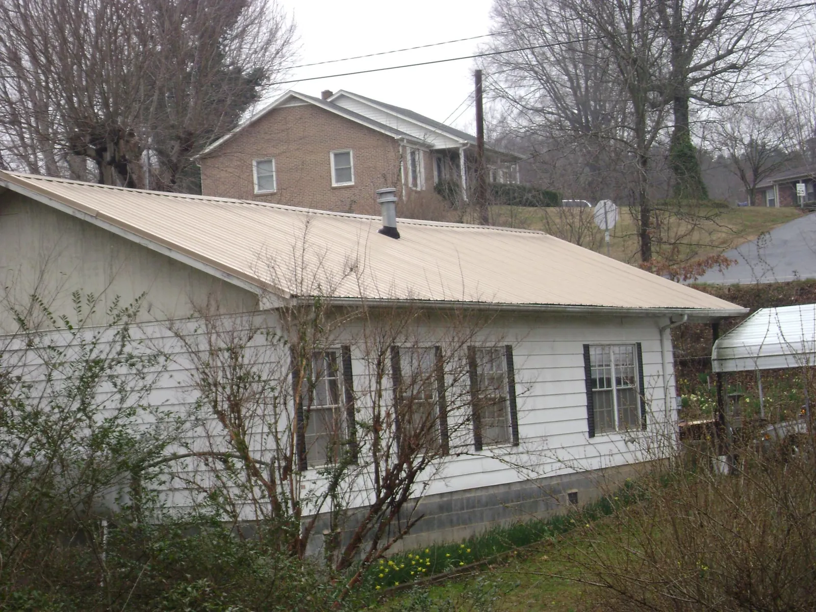 Tan metal roof on a white sided house set into a hillside — Commercial Roofing by Roofing Brothers in Pacolet